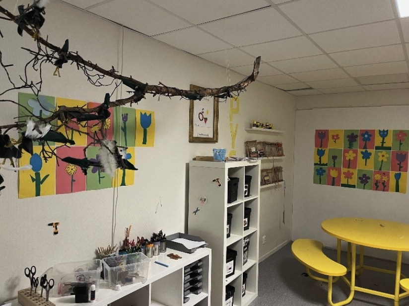 Fritidshem på Alnöitskolan med kreativt material, barnens blomsterbilder på väggarna och en gul sittgrupp.